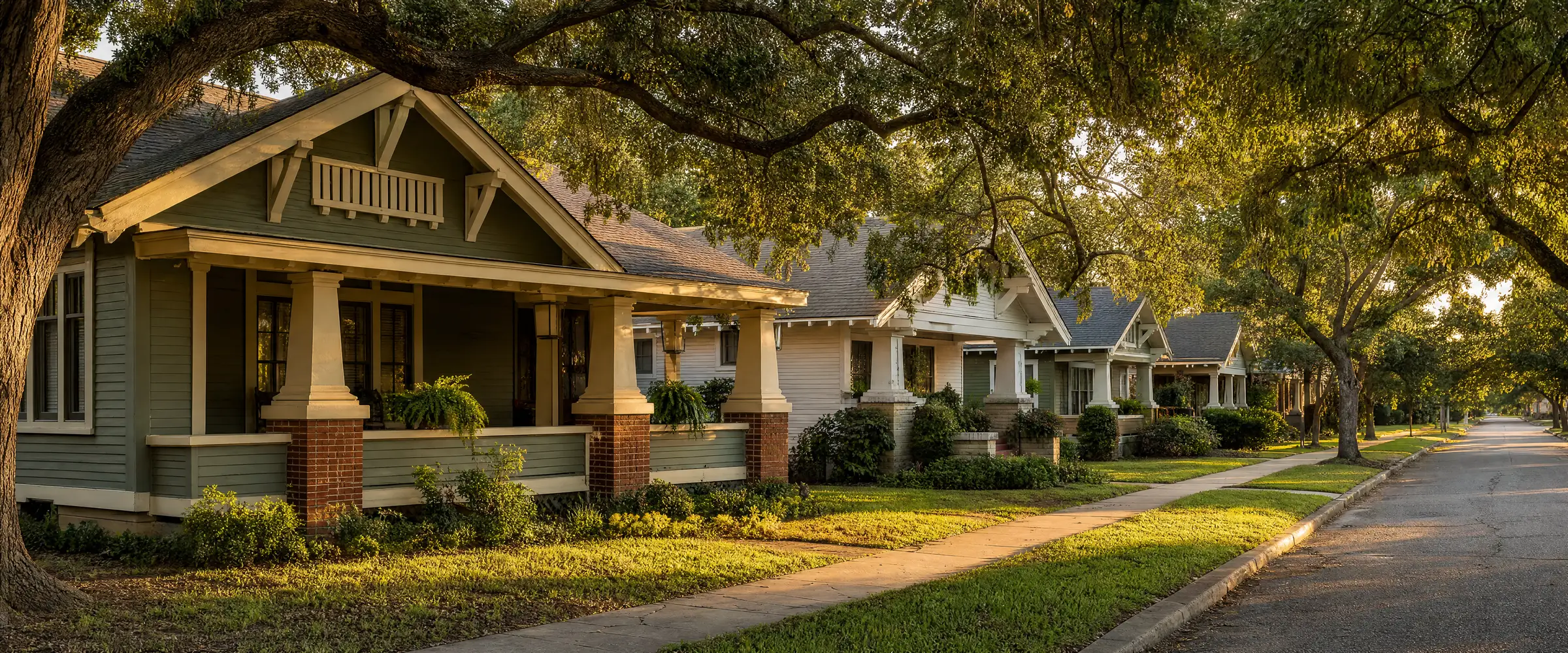 A residential street of early-twentieth-century craftsman bungalows with deep front porches, under mature trees in late afternoon light.
